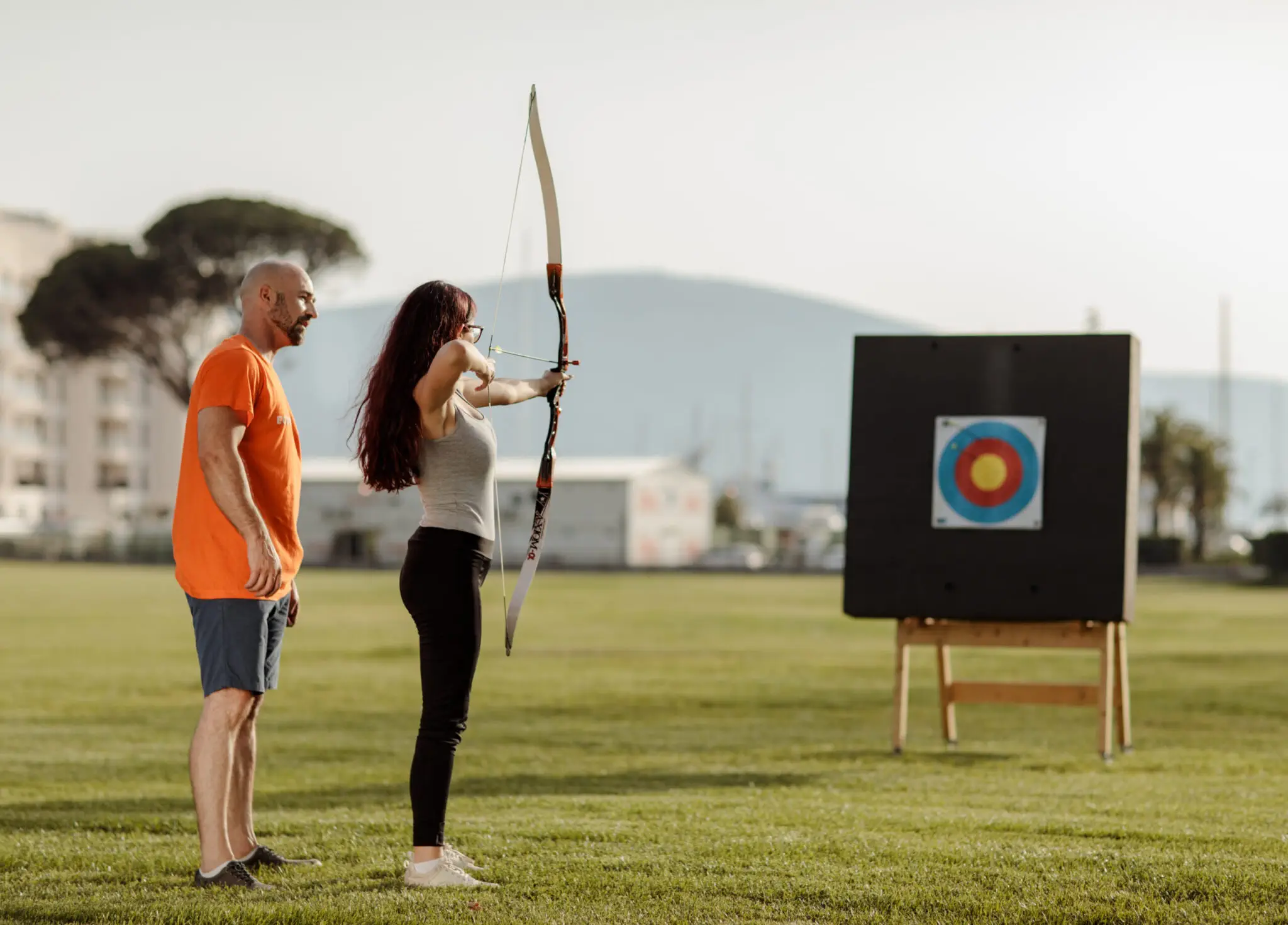 Guy teaching girl archery skills